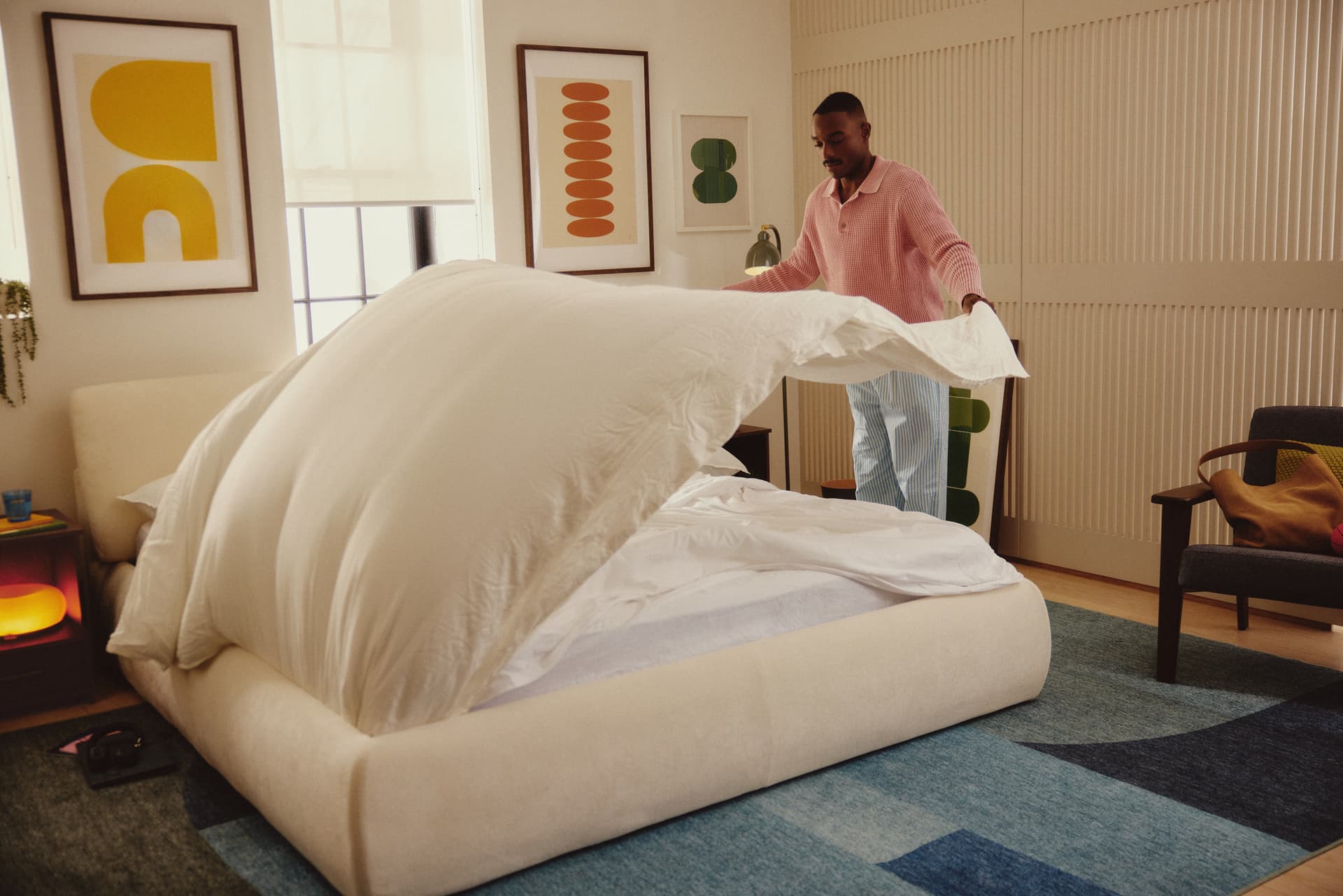 Personne soulevant une couette sur un lit Ara crème dans une chambre colorée