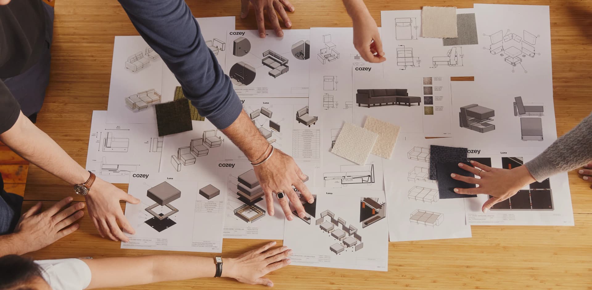 Hands of the Cozey design team around a table covered with furniture sketches