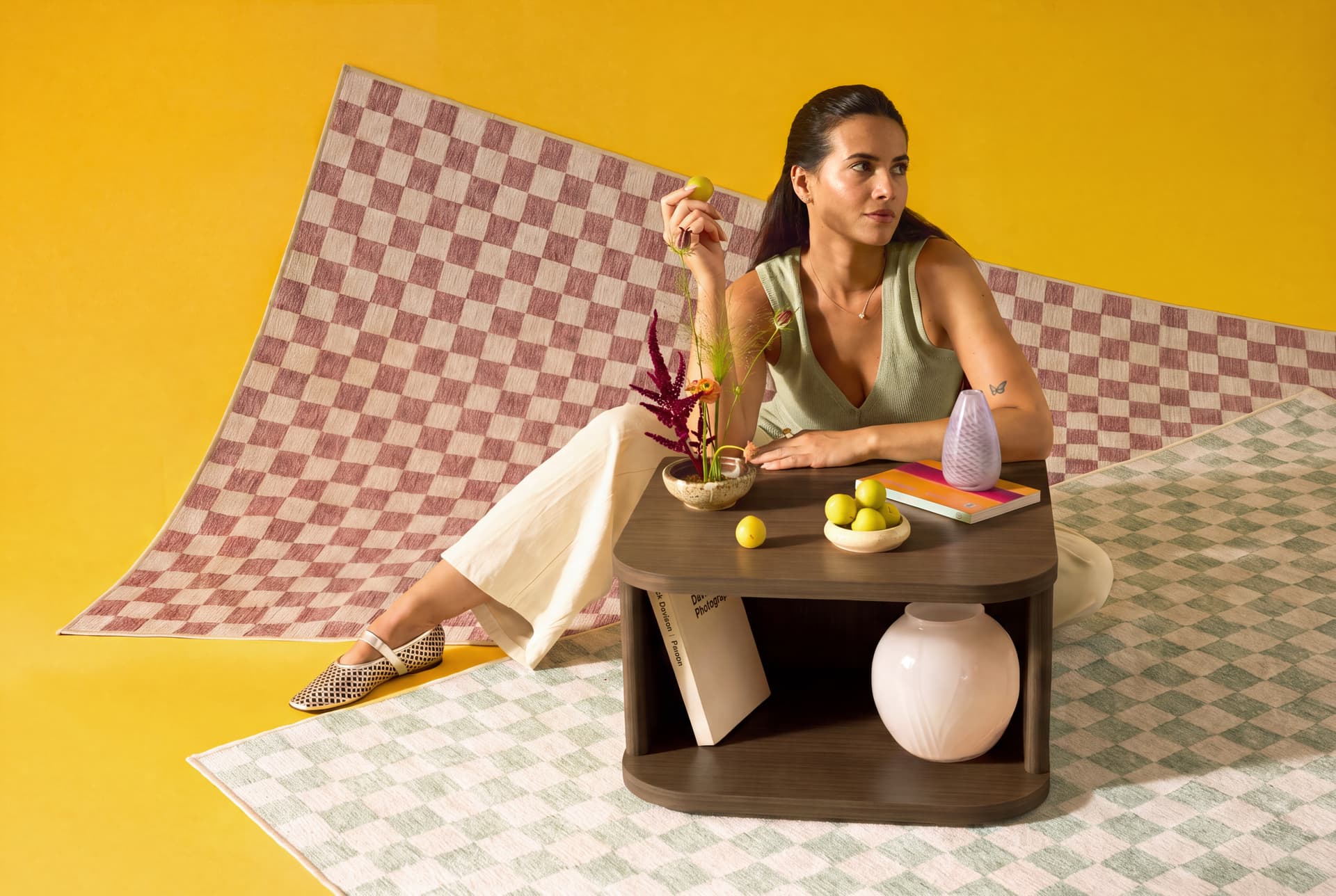 Woman at a walnut side table on a checkered washable rug against a yellow backdrop