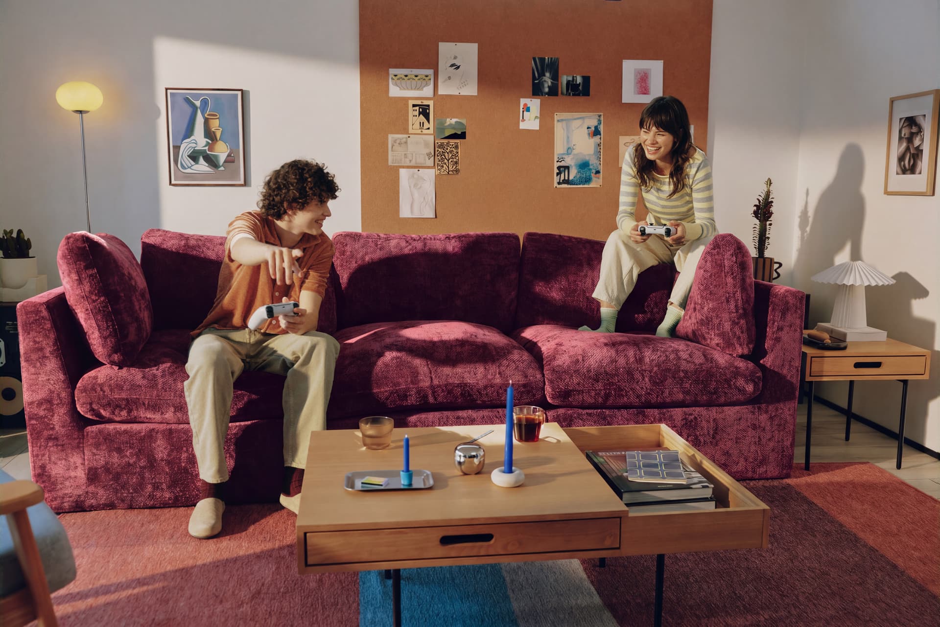 Two friends playing video games on a bordeaux Cozey sofa