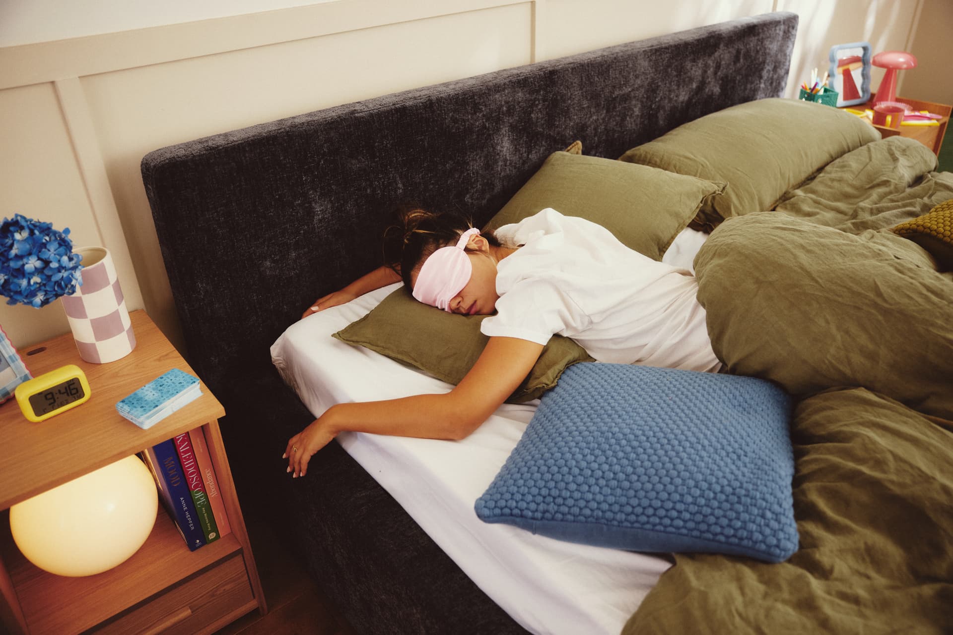 Person sleeping in an Ara bed with a dark upholstered headboard and olive bedding
