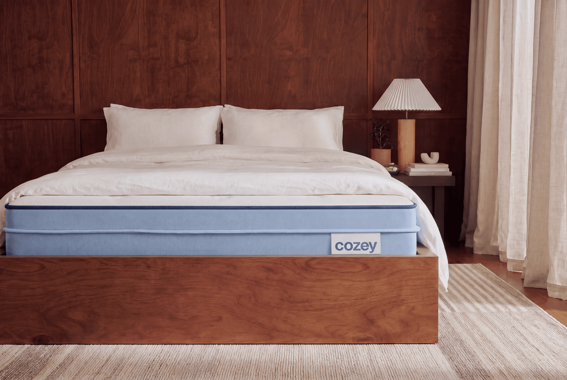Cozey Hybrid mattress on a wooden bed frame in a bedroom with a walnut-panelled wall